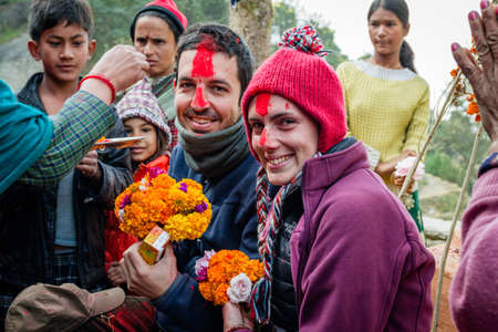 Two young travellers are greeted with flowers, a bindi on their forehead and some treats by nepali villagers in the mountains of Dhuskun, Nepalのeditorial素材