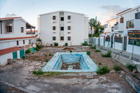 Community terrain with swimming pool in the middle. The pool has no water, the property is abandoned and looks severely damaged. Plants and weeds are growing at their will since nobody looks after the place any moreの写真素材