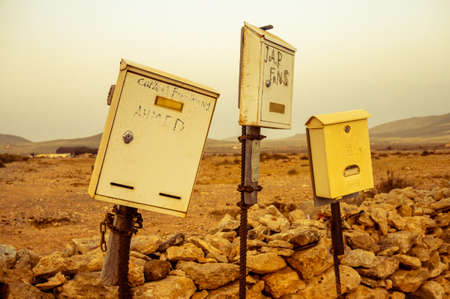 A group of mail boxes stand before a desertic abandoned landscape in the middle of nowhere. They look home made, shabby, worn out and left behind, as if nobody uses them any more. Fuerteventura, Spainの写真素材