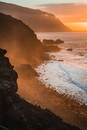 Waves hit rocky coastline at sunset, beautiful layered cliffs with mist rolling in from ocean. Atmospheric view sightseeingの写真素材