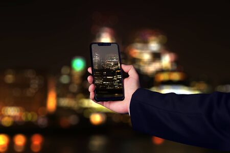 Businessman taking a picture of the London skyline out of focus and at nightの写真素材