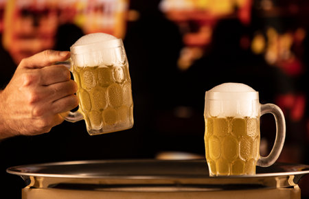 two mugs of cold beer with foam on a tray in a bar