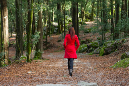 Young woman walking away alone on a forest path wearing a red overcoat Young woman walking away alone on a forest path wearing a red overcoat