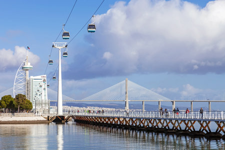Lisbon, Portugal - February 01, 2015: People practicing sports on the Passeio Ribeirinho over the Tagus River. Vasco da Gama Tower and Bridge, Myriad Hotel and aerial tramway. Park of Nationsのeditorial素材