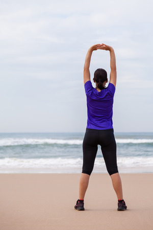 Female athlete warming up and stretching the upper body before running at the beach on an Autumn day.の写真素材