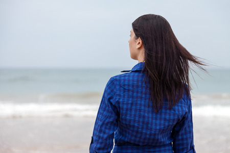 Lonely and depressed woman standing in front of the sea in a deserted beach on an Autumn day.の写真素材