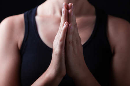 Low key, close up of hands of a faithful woman praying, with hands folded and palms together in worship to god, on a black background. Concept for religion, faith, prayer and spirituality.の写真素材