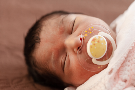 Close up portrait of a cute two weeks old newborn baby girl wearing soft pink knit clothes, sleeping peacefully with a pacifier, aka dummy or sootherの写真素材