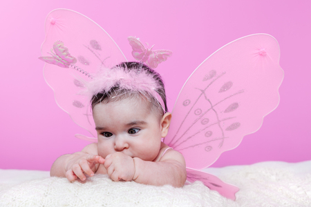 Cute, pretty, happy, chubby baby girl curious about her hands crossing eyes to focus, with pink butterfly wings and headband with butterflies. Four months oldの写真素材