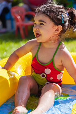 Cute, happy, smiling toddler baby girl, playing in colorful inflatable backyard garden swimming pool in hot summer day. Thirteen months oldの写真素材