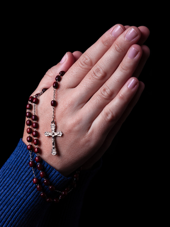 Female praying holding a rosary with Jesus Christ in the cross or Crucifix on black backgroundの写真素材