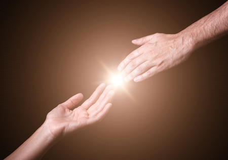 Reaching and touching hands. Bright light star flare with touching fingertips. Concept for salvation, rescue, friendship, guidance. Black background.の写真素材