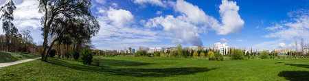 Panorama of a large empty green grass lawn field, with a view of the city in Parque da Devesa Urban Park. Blue sky with large white clouds. Vila Nova de Famalicao, Portugalのeditorial素材