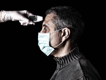 man having the fever measured or taken with digital thermometer by nurse. Pandemic or epidemic and scary, fear or danger concept. Protection for biohazard like COVID-19 aka Coronavirusの写真素材