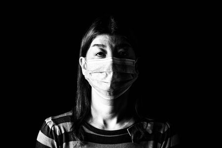 Woman with surgical mask. Pandemic or epidemic and scary, fear or danger concept. Protection for biohazard like COVID-19 aka Coronavirus. Black and White. Black Backgroundの写真素材