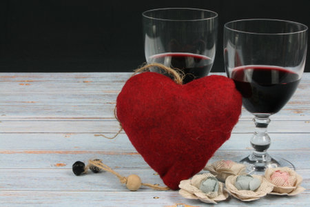 Romantic scene of two glasses of red wine and a red heart on a vintage wooden background, with space to place textの写真素材