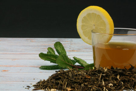 Green tea cup with a lemon wedge and mint leaves, accompanied by bulk tea on a vintage wood backgroundの写真素材