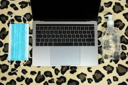 Top view of a computer accompanied by a mask and hydroalcoholic gel on a jaguar skin background