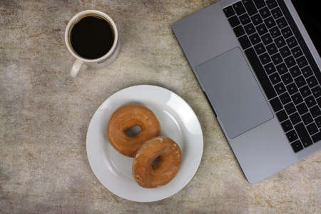 Top view of a computer accompanied by a tablet, a mobile phone and coffee with scones on an abstract backgroundの写真素材