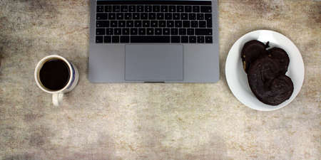 Top view of a computer accompanied by a tablet, a mobile phone and coffee with scones on an abstract backgroundの写真素材