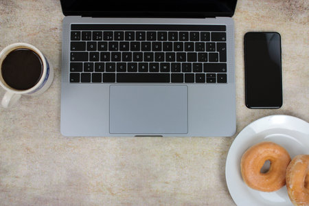 Top view of a computer accompanied by a tablet, a mobile phone and coffee with scones on an abstract backgroundの写真素材