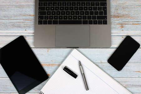 Top view of a computer accompanied by a tablet, a mobile phone and office supplies on vintage wooden backgroundの写真素材
