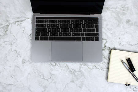 Top view of a computer accompanied by a tablet, a mobile phone and office supplies on marble...