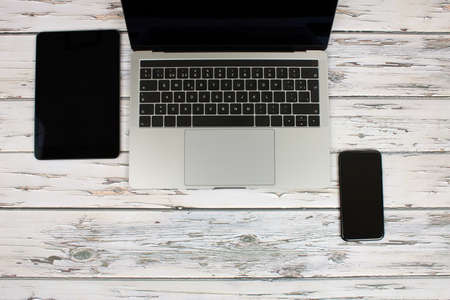 Top view of a computer accompanied by a tablet, a mobile phone and office supplies on vintage wooden backgroundの写真素材