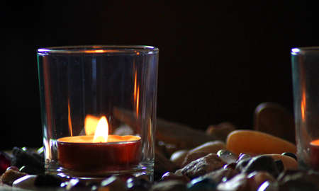 Burning candles in a glass on a black background with stones.の写真素材