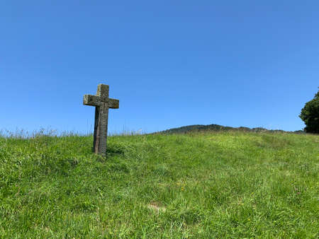 Old wooden cross on a hillside with green grass and blue skyの写真素材