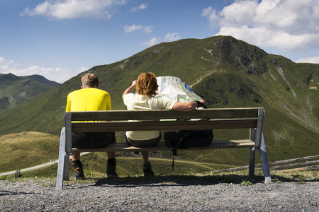 Couple sitting on bench woman looking at map in idyllic summer Alps mountains landscapeの写真素材