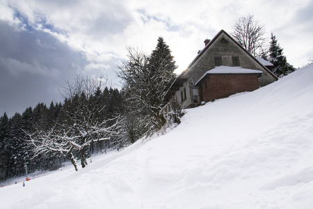 Snow covered house in a frosty mountains country in sunny winter dayの写真素材