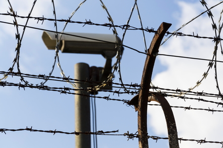 Security camera behind barbed wire fence stretched around prison wallsの写真素材