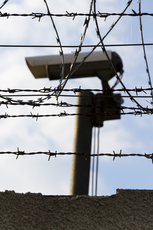 Security camera behind barbed wire fence stretched around prison wallsの写真素材
