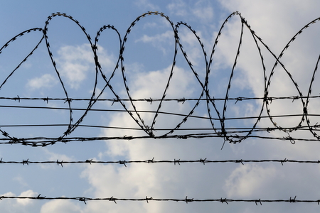 Prison wall barbed wire fence detail with blue sky in backgroundの写真素材