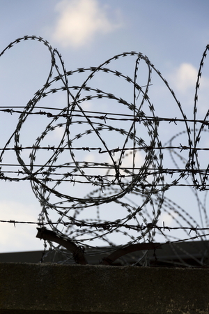 Prison wall barbed wire fence detail with blue sky in backgroundの写真素材