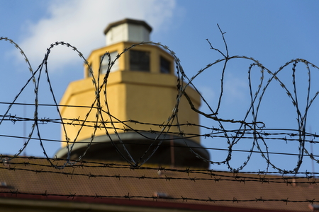 Guarding tower behind barbed wire fence stretched around prison wallsの写真素材