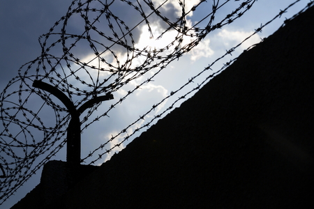Dramatic clouds behind barbed wire fence on a prison wallの写真素材