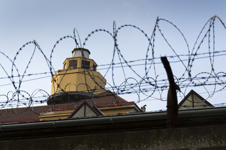 Guarding tower behind barbed wire fence stretched around prison wallsの写真素材
