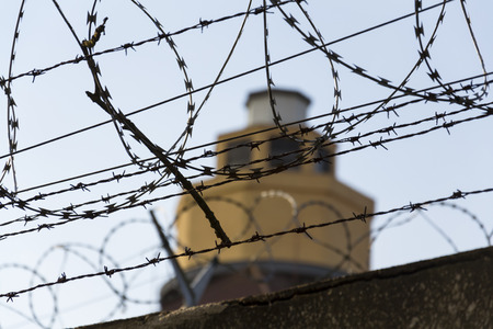 Guarding tower behind barbed wire fence stretched around prison wallsの写真素材