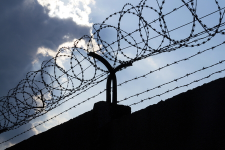 Dramatic clouds behind barbed wire fence on a prison wallの写真素材