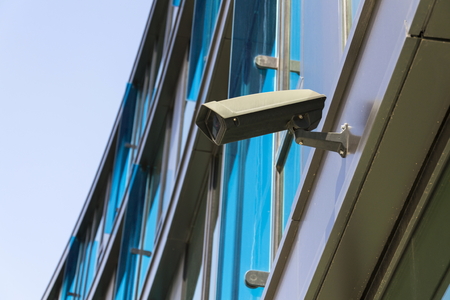 Grey security camera attached to wall blue windows in backgroundの写真素材