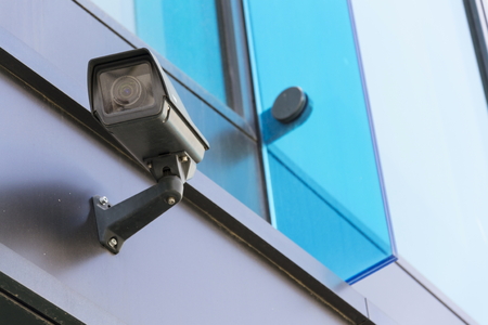 Grey security camera attached to wall blue windows in backgroundの写真素材