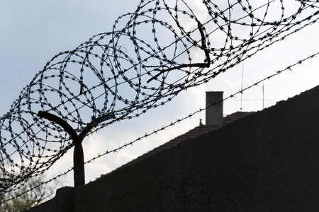 Barbed wire fence around prison walls blue sky in backgroundの写真素材