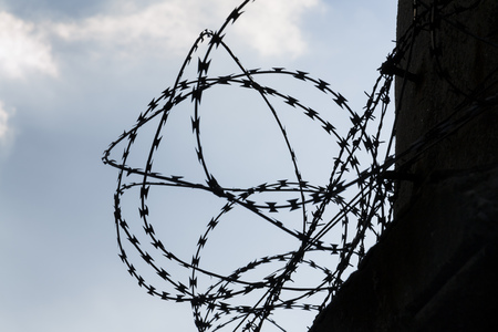 Barbed wire fence around prison walls blue sky in backgroundの写真素材