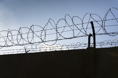 Barbed wire fence around prison walls blue sky in backgroundの写真素材