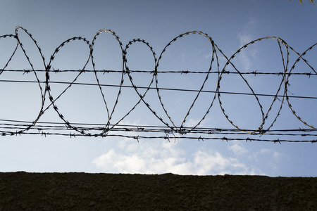 Barbed wire fence around prison walls blue sky in backgroundの写真素材