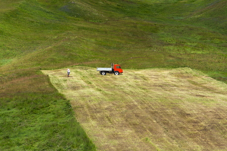 Man rakes hay with truck on steep hillside, Livigno, Italyの写真素材