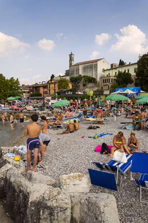 DESENZANO DEL GARDA, ITALY - JULY 30: People sunbathing on beach on 30 July 2016 in Desenzano del Garda, Italy.のeditorial素材