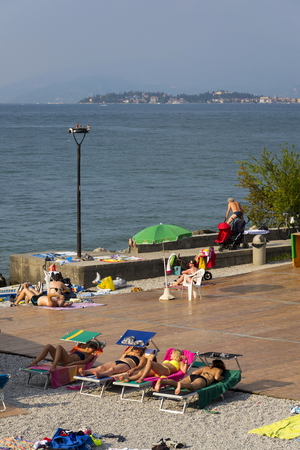 DESENZANO DEL GARDA, ITALY - JULY 30: People sunbathing on beach on 30 July 2016 in Desenzano del Garda, Italy.のeditorial素材